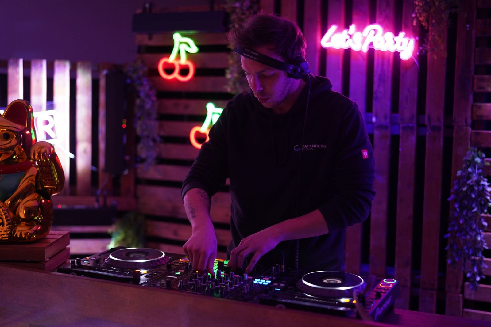 Milo Sava mixing between neon cherries and a pink Let's Party sign