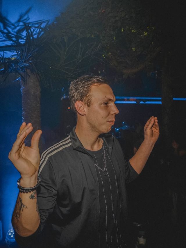 Milo Sava under palm leaves in blue light
